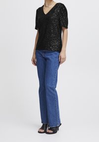 Svart paljettopp med V-ringning, kort puffärmar, kombinerat med blå utsvängda jeans och svarta högklackade sandaler.