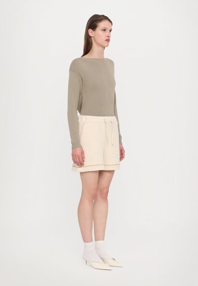 Khaki langermet genser med rund hals, kombinert med beige shorts med elastisk midje og lys orange sømmer, samt to sidelommer.