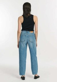 Jasnoniebieskie dżinsy z wysokim stanem i prostą nogawką, z tylnymi kieszeniami oraz brązową skórzaną łatą w pasie. W połączeniu z czarnym topem na ramiączkach.