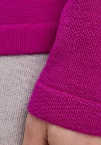 Fuchsia gebreide stof met een geribde manchet, contrasterend tegen een lichtgrijze achtergrond. Gladde textuur, flexibel en nauwsluitend ontwerp.