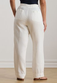 Fehér lenvászon bőszárú nadrág sima textúrával, két hátsó zsebbel, amelyek patenttal záródnak, és laza fazonú.