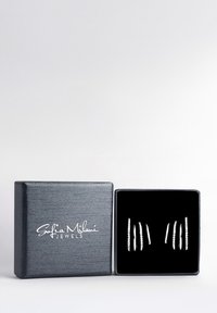 Boucles d'oreilles en argent en présentation dans une boîte tapissée de velours noir avec un extérieur texturé gris foncé et une marque blanche.