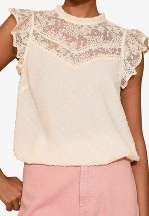 Roomkleurige mouwloze blouse met kanten inzetstuk en gerimpelde randen, gecombineerd met een hooggetailleerde lichtroze broek.