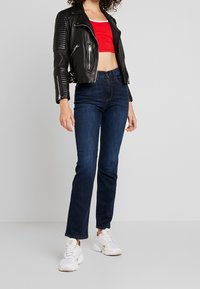 Svart läderbikerjacka med ribbade detaljer, röd kort topp, mörkblå skinny jeans och vita sneakers.