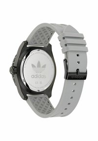 Sivo uro z teksturiranim trakom, ki ima črn ohišje in graviran logotip Adidas na hrbtni strani. Oblikovanje je športno in moderno.