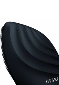 Brosse à cheveux noire avec un design incurvé et ondulé et un matériau doux au toucher. Présente des poils fins le long d'un bord et un détail de logo en relief.