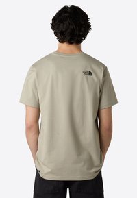 T-shirt corti a maniche con collo rotondo in beige chiaro, con un logo nero stampato sulla parte superiore della schiena. Texture liscia e vestibilità casual.