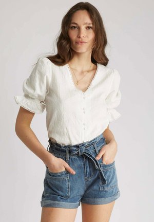 Blouse blanche texturée avec des manches courtes bouffantes et un bouton à l'avant. Associée à un short en denim taille haute avec des revers et des poches avant.
