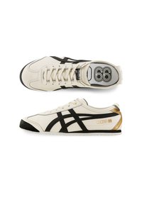 White leather sneakers feature black accents, a rubber sole, a gold "MEXICO 66" detail, and a sleek design with a lace-up closure.