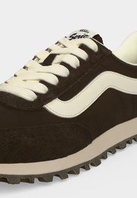 Кафяво маратонка Vans с бяла ивица и дебели бели връзки, текстурирана подметка и лого "Vans Senior" на езика.