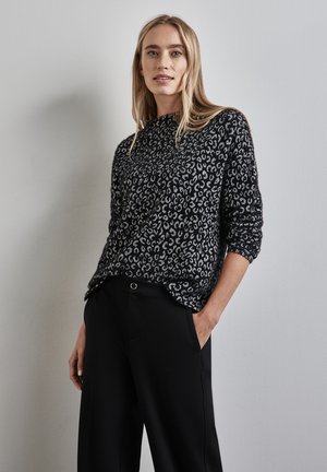 Black and white sweater with a leopard print pattern, featuring long sleeves and a relaxed fit, paired with high-waisted black pants.