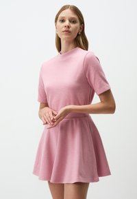 Abito corto rosa a maniche corte con scollatura alta, corpetto attillato e gonna svasata. Realizzato in un tessuto morbido e texturizzato.