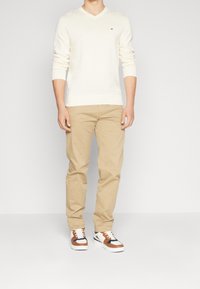 Maglione a scollo a V crema, chinos beige e sneakers multicolori. Il maglione ha maniche lunghe; i pantaloni sono a gamba dritta; le sneakers hanno suole in gomma bianca.