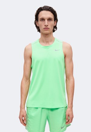 Homme portant un haut de sport sans manches vert clair et un short assorti, debout devant un fond clair uni.