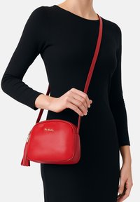 Rode leren schoudertas met een ronde vorm, gouden hardware en een franjesaccent. Gladde textuur, ritssluiting en verstelbare schouderband.