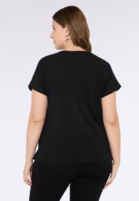 Camiseta negra de manga corta con cuello redondo, que presenta puños enrollados y un ajuste relajado. Tejido suave con detalles de costura.