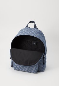 Sac à dos à motif bleu avec un intérieur noir, ouverture zippée et poche avant. Le matériau a une texture lisse avec un éclat subtil.