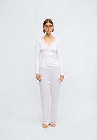 Biele tričko s dlhými rukávmi a čipkovaným výstrihom, v kombinácii s svetlošedými nohavicami. Tkanina pôsobí mäkko a pohodlne s voľným strihom. Čipkované ozdoby na manžetách.