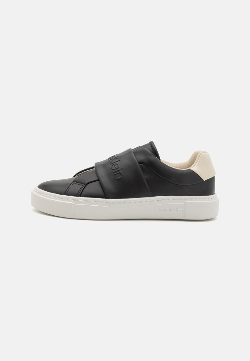 Calvin Klein svarte slip-on sneakers med en teksturert læroverdel, elastisk stropp og kontrasterende hvit gummisåle. Detaljert merking er synlig.