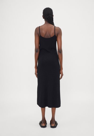 Schwarzes, figurbetontes, ärmelloses Midikleid mit dünnen Trägern. Hergestellt aus glattem Material, hat es ein einfaches Design und eine gerade Silhouette, die durch flache Sandalen ergänzt wird.