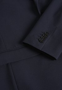 Marineblaues maßgeschneidertes Sakko mit einer glatten Textur, schlankem Design und fünf schwarzen Knöpfen entlang des Ärmeldetails.