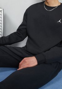 Felpa nera e pantaloni abbinati in tessuto morbido. Presenta un piccolo logo bianco sul petto e una vestibilità rilassata. Design semplice, senza fantasie.