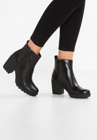 Bottes noires à la cheville en cuir lisse, talon bloc haut, fermetures éclair latérales et semelles en caoutchouc texturé pour une bonne traction.