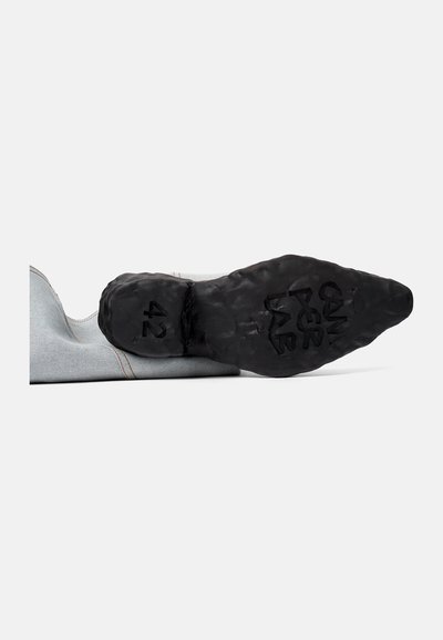 Zapato de denim con una parte superior suave de color gris, costuras naranjas en contraste y una suela de goma negra texturizada que presenta el tamaño '42' grabado en ella.