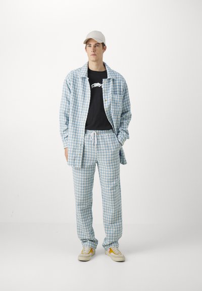 Blå og hvit rutete flanellskjorte og matchende bukser, bomullsblanding; kombinert med en svart grafisk t-skjorte og beige caps. Sneakers med detaljer.