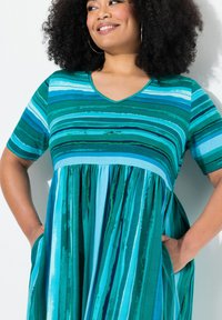 Pasiasta sukienka w różnorodnych odcieniach teal i niebieskiego, z dekoltem w serek, krótkimi rękawami i rozkloszowanym dołem z kieszeniami. Gładka tekstura.