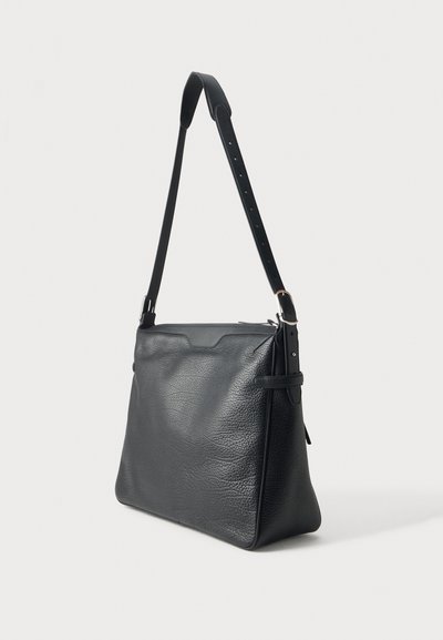 Sac à bandoulière noir en cuir grainé, avec une longue bandoulière réglable, une boucle argentée et un détail de sangle sur le côté, présenté sur un fond clair.