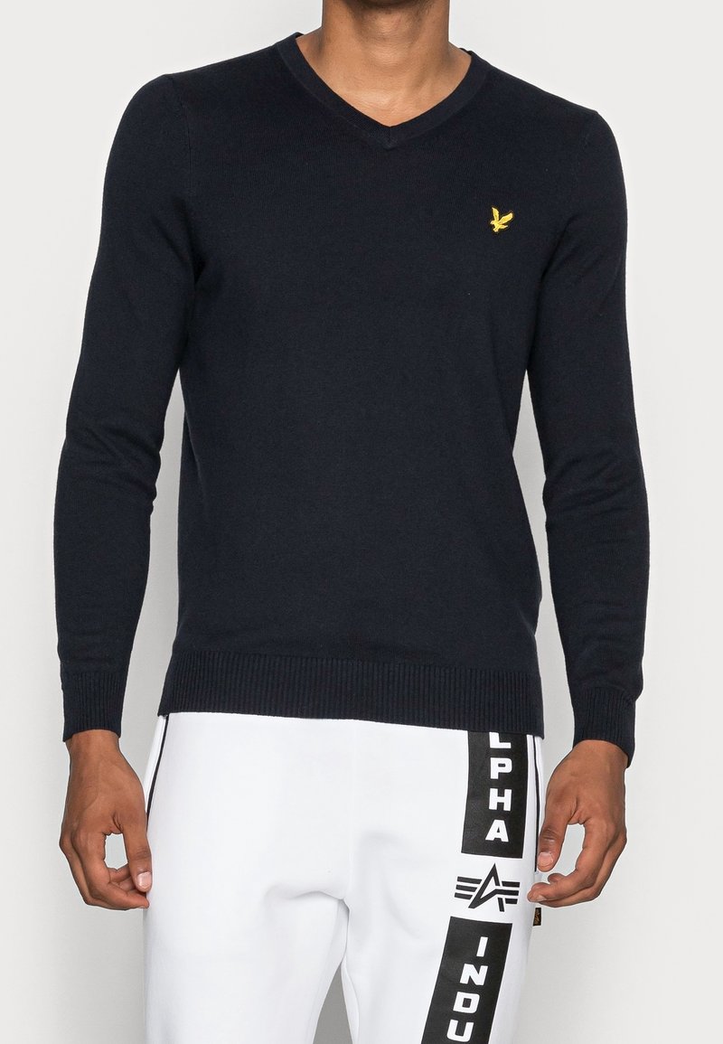 Maglione in maglia blu navy con scollo a V e maniche lunghe. Presenta polsini e orlo a coste, con un piccolo emblema giallo sul petto.