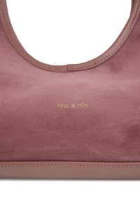 Sac en daim rose pâle avec une bordure en cuir lisse. Logo doré embossé "nat & nin" sur le devant. Forme arrondie, design minimaliste.