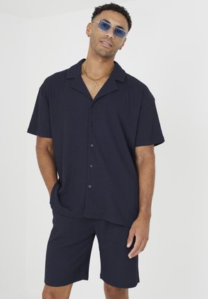 Chemise à manches courtes bleu marine à boutonner avec une coupe décontractée, assortie à un short. Tissu léger avec une surface texturée.
