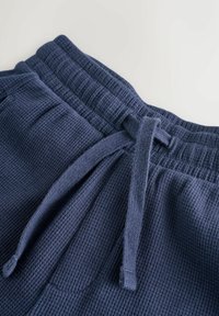 Pantaloni jogger blu navy in tessuto strutturato, con fascia in vita a coste e dettaglio con coulisse per la regolazione.
