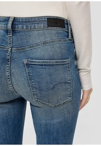 Dark blue denim jeans with a high waist, featuring a black label on the back, two rear pockets, and a subtle faded texture.