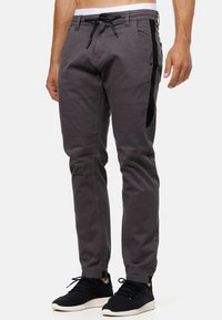 Pantalones de mezcla de algodón grises con paneles laterales negros, ajuste tapered y cintura con cordón ajustable. Combinados con zapatillas deportivas negras.