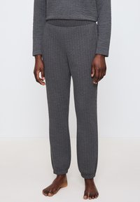 Graue gerippte Lounge-Hosen mit glatter Textur, ausgestattet mit einem elastischen Bund und schmal zulaufenden Bündchen an den Knöcheln, ohne sichtbare Muster oder Akzente.