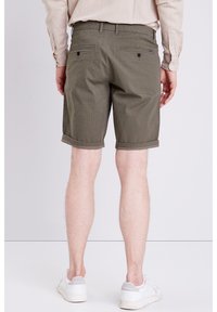 Olivgröna shorts med ett strukturerat mönster, uppvikta fållar och två bakfickor. Kombinerat med vita sneakers och en beige tröja.