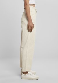Beige corduroy broek met wijde pijpen en hoge taille, met zijzakken en zichtbare stiksels. Gecombineerd met witte sneakers voor een casual uitstraling.