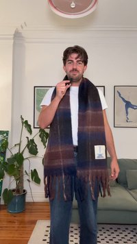 Vuna šal s tamno plavim i smeškim horizontalnim prugama, resastim ivicama i kvadratnom etiketom s grafičkim dizajnom. Mekana tekstura.