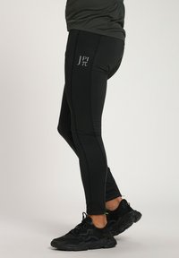 Schwarze Sportleggings mit taillierter Passform, versehen mit einem logo in hellgrau an der Seite, aus einem glatten, dehnbaren Material gefertigt.