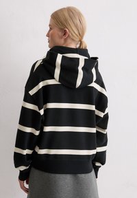 Black and white striped hoodie with a large hood, soft texture, slightly oversized fit, and ribbed cuffs and hem.