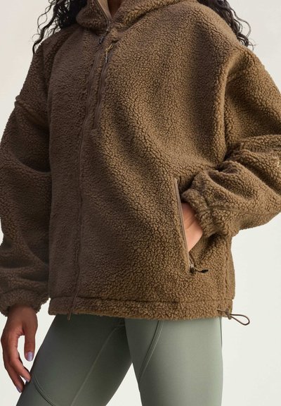 Brown fleece jacket with a hood, featuring a zippered front, side pockets, and elastic cuffs. The texture is soft and cozy.