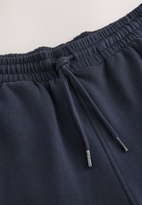 Donkerblauwe joggingbroek met een elastische tailleband met trekkoord, een gladde textuur en metalen accenten aan de uiteinden van het trekkoord.