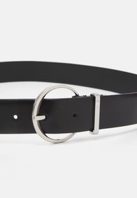 Curea din piele neagră cu o cataramă rotundă din argint și un închizător rectangular cu logo-ul "Calvin Klein".Textură netedă, ajustabilă.