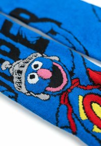 Calzini blu con un personaggio dei cartoni animati che indossa un mantello rosso, occhi grandi e una bocca sorridente, design tessile con accenti neri e gialli.