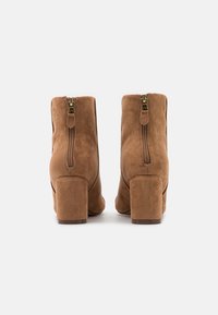 Bottines en daim marron avec un bout arrondi, un talon bloc de hauteur moyenne et une fermeture éclair à l'arrière. Texture douce et design sans coutures.