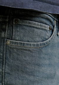 Blå denimjeans med en klassisk femficksdesign, med mörka metallknappar, synlig sömnad och en lätt textur.