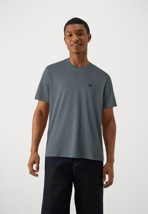Camiseta de algodón gris con mangas cortas y cuello redondo, que presenta un pequeño logo en el pecho. Textura suave y ajuste clásico.